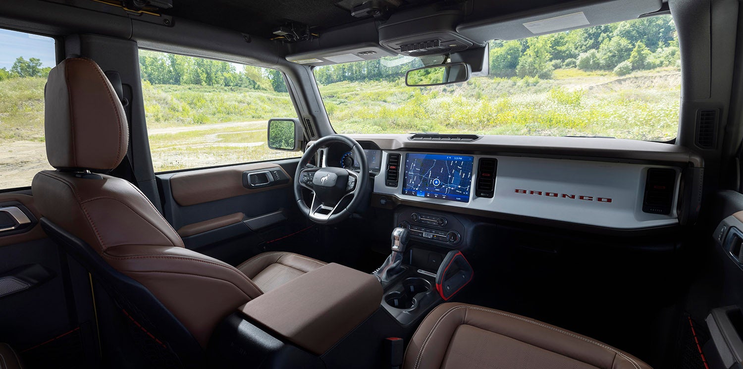 The interior of a 2023 Ford Bronco Heritage Edition, featuring white and red plaid cloth seats, a white dashboard, and a large touchscreen infotainment system.