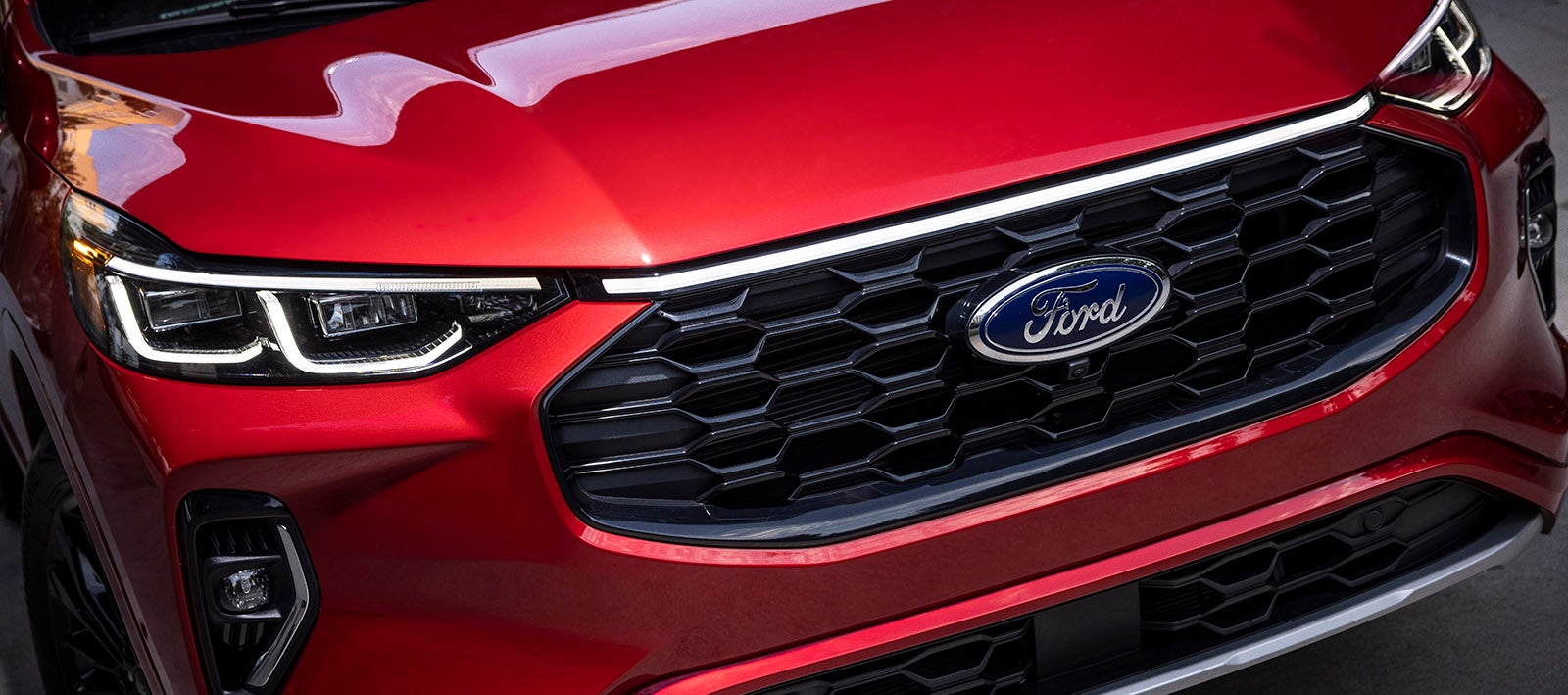 "Close-up view of the front grille and headlights of a red Ford vehicle, showcasing the Ford logo prominently centered on the black honeycomb grille design."